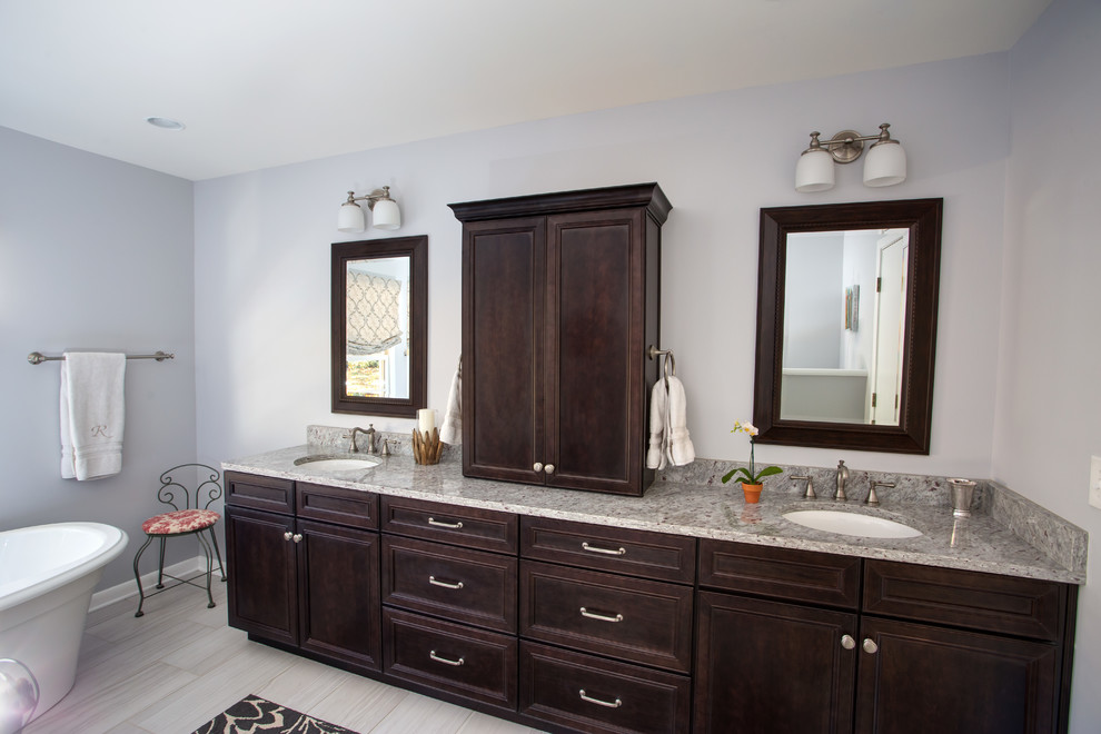 Photo of a mid-sized traditional master bathroom in Birmingham with furniture-like cabinets, dark wood cabinets, a freestanding tub, an alcove shower, a two-piece toilet, gray tile, porcelain tile, blue walls, porcelain floors, an undermount sink, granite benchtops, grey floor, a hinged shower door and multi-coloured benchtops.