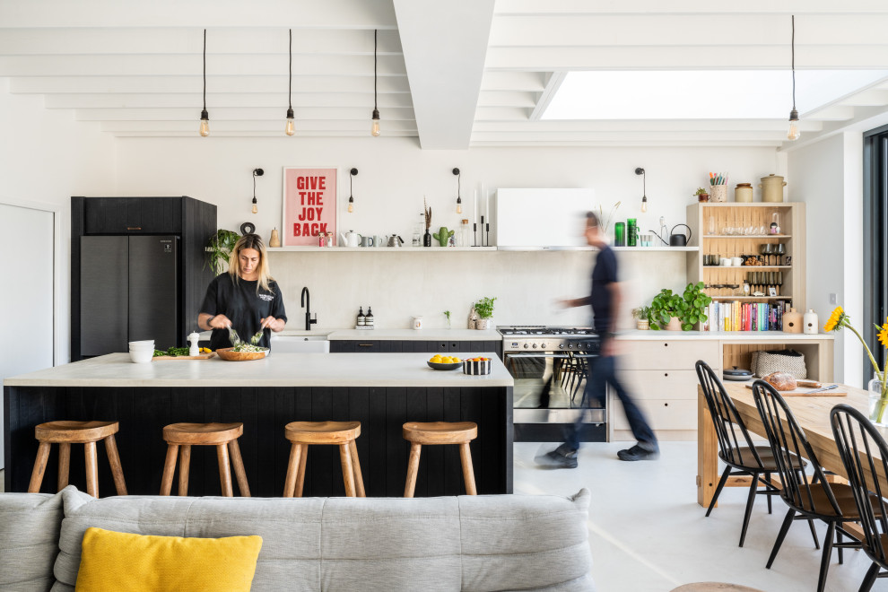 This is an example of a contemporary galley open plan kitchen in London with a belfast sink, flat-panel cabinets, black cabinets, black appliances, an island, white floors, white worktops and exposed beams.