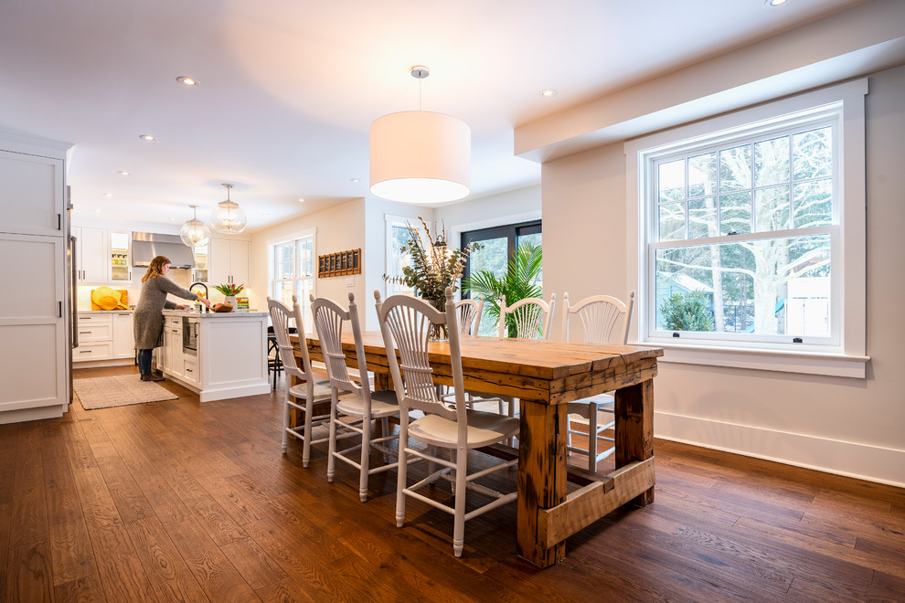 This is an example of a mid-sized country kitchen/dining combo in Toronto with beige walls, medium hardwood floors, a hanging fireplace, a metal fireplace surround and brown floor.