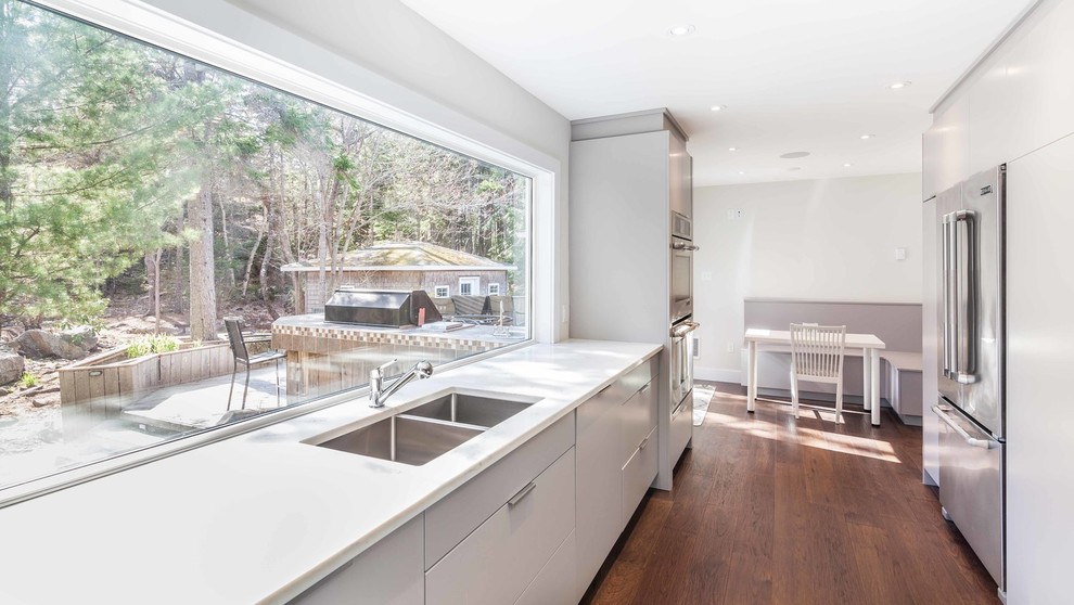 Large minimalist u-shaped dark wood floor and brown floor eat-in kitchen photo with a double-bowl sink, flat-panel cabinets, gray cabinets, quartzite countertops, gray backsplash, stone tile backsplash, stainless steel appliances and a peninsula