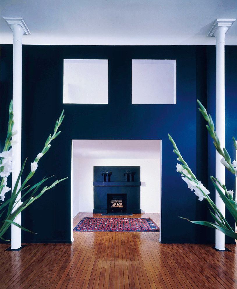 This is an example of a small loft-style family room in New York with blue walls, dark hardwood floors, a corner fireplace, a plaster fireplace surround and brown floor.