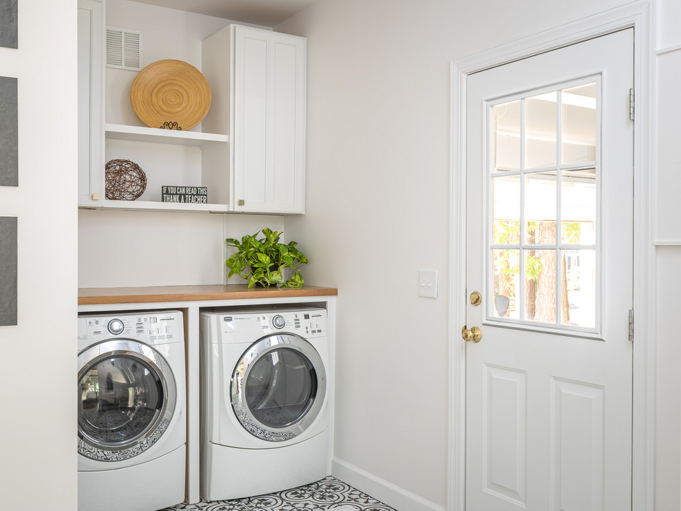 Photo of a mid-sized country utility room in Raleigh with a farmhouse sink, white cabinets, quartzite benchtops, white walls, porcelain floors, a side-by-side washer and dryer, multi-coloured floor and brown benchtop.