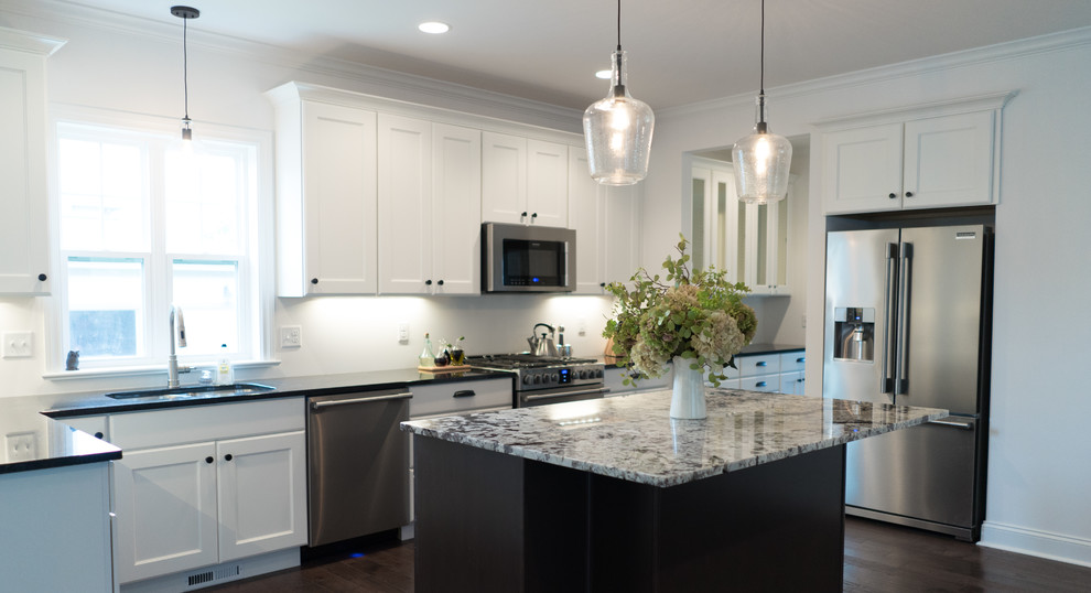 Open concept kitchen - mid-sized transitional l-shaped dark wood floor open concept kitchen idea with an undermount sink, shaker cabinets, white cabinets, granite countertops, gray backsplash, stainless steel appliances and an island