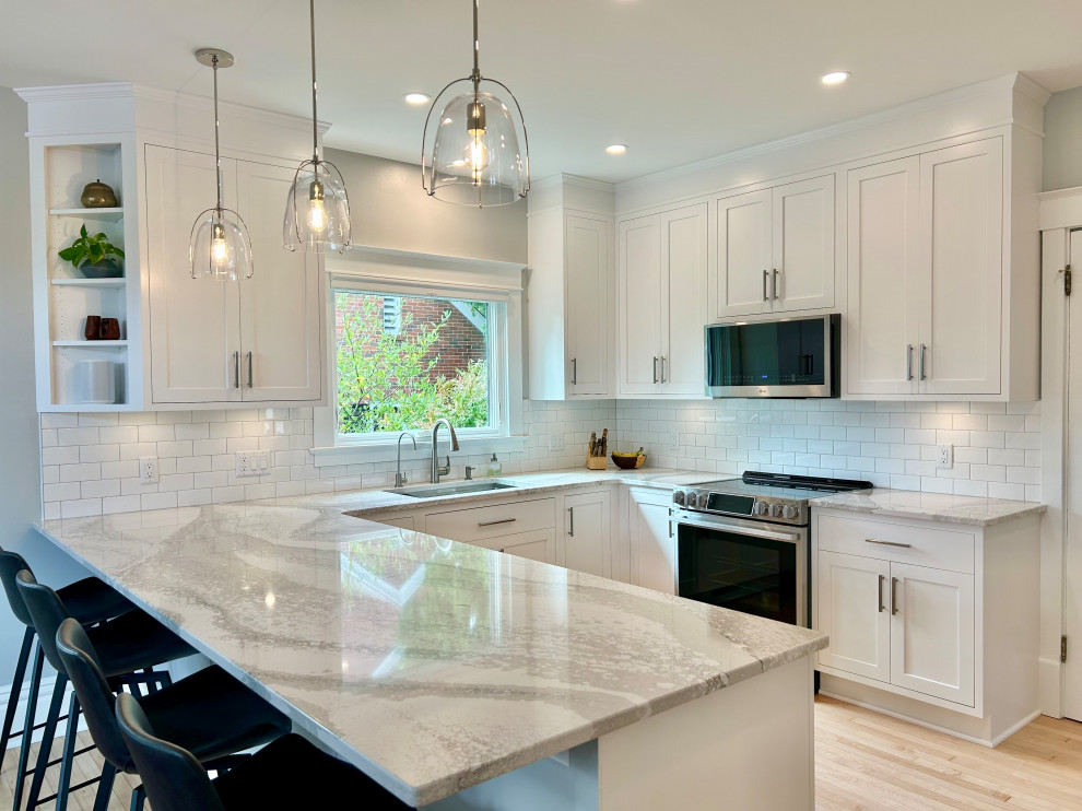 Mid-sized transitional u-shaped light wood floor and beige floor open concept kitchen photo with an undermount sink, beaded inset cabinets, white cabinets, quartz countertops, white backsplash, ceramic backsplash, stainless steel appliances, a peninsula and white countertops