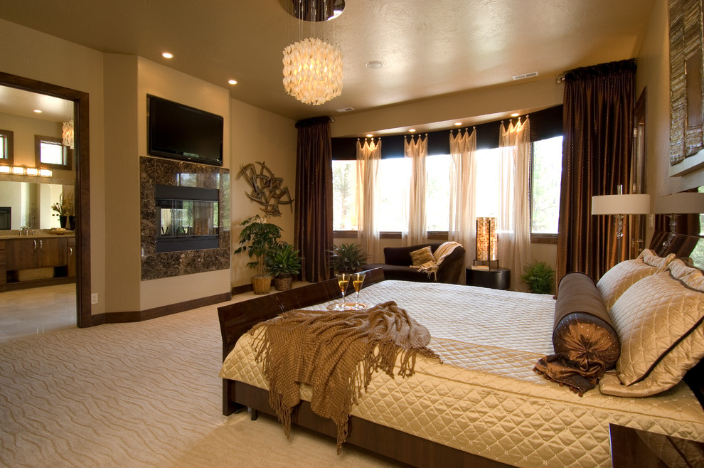 This is an example of a large contemporary master bedroom in Denver with beige walls, carpet, a two-sided fireplace, a stone fireplace surround and beige floor.
