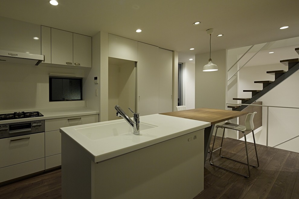Small modern galley open plan kitchen in Tokyo with an undermount sink, beaded inset cabinets, white cabinets, solid surface benchtops, white splashback, white appliances, plywood floors, with island and brown floor.