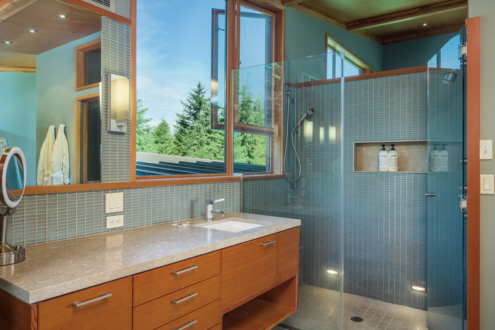 This is an example of a mid-sized modern master bathroom in Seattle with flat-panel cabinets, medium wood cabinets, a curbless shower, a wall-mount toilet, blue tile, limestone, blue walls, limestone floors, an undermount sink and limestone benchtops.
