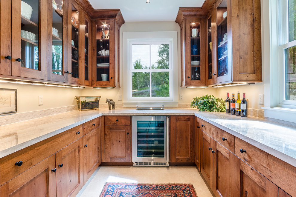 This is an example of a large traditional l-shaped kitchen pantry in Denver with glass-front cabinets, medium wood cabinets, marble benchtops, beige splashback, stone tile splashback, stainless steel appliances and travertine floors.