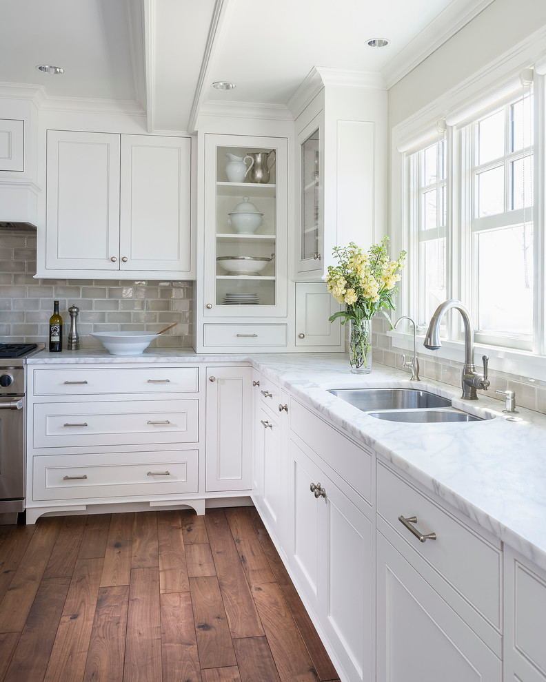 This is an example of a mid-sized traditional l-shaped kitchen in Minneapolis with an undermount sink, recessed-panel cabinets, white cabinets, marble benchtops, grey splashback, ceramic splashback, dark hardwood floors, with island and stainless steel appliances.