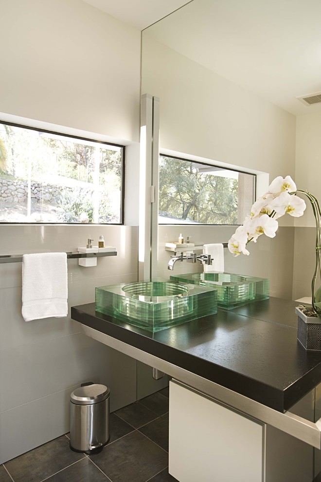This is an example of a modern powder room in San Francisco with a vessel sink, gray tile and brown benchtops.