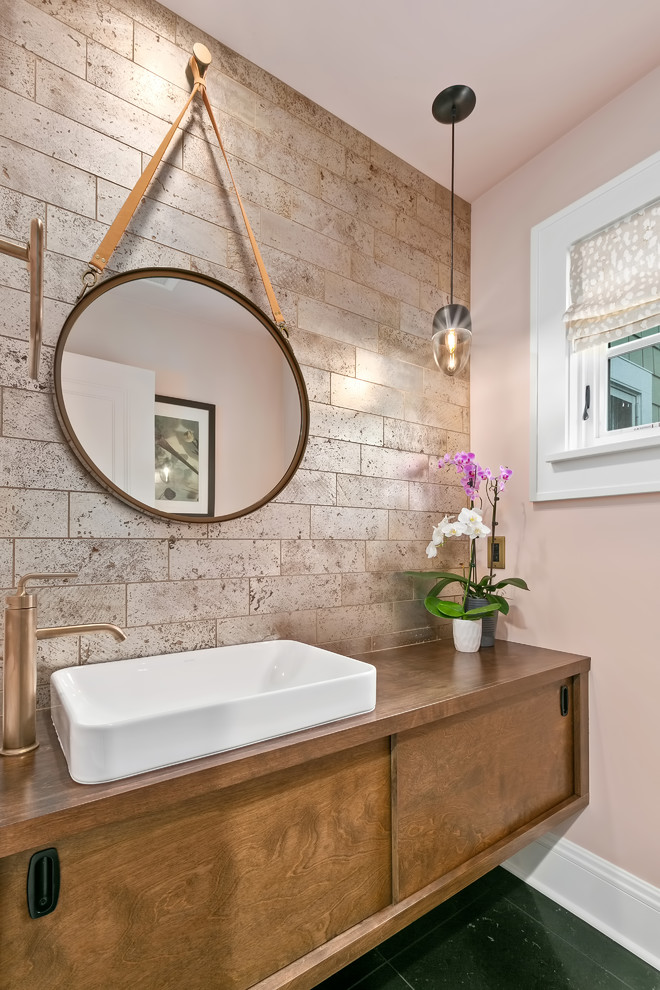 Inspiration for a small transitional powder room in Minneapolis with flat-panel cabinets, medium wood cabinets, pink walls, slate floors, a vessel sink, wood benchtops, black floor and brown benchtops.