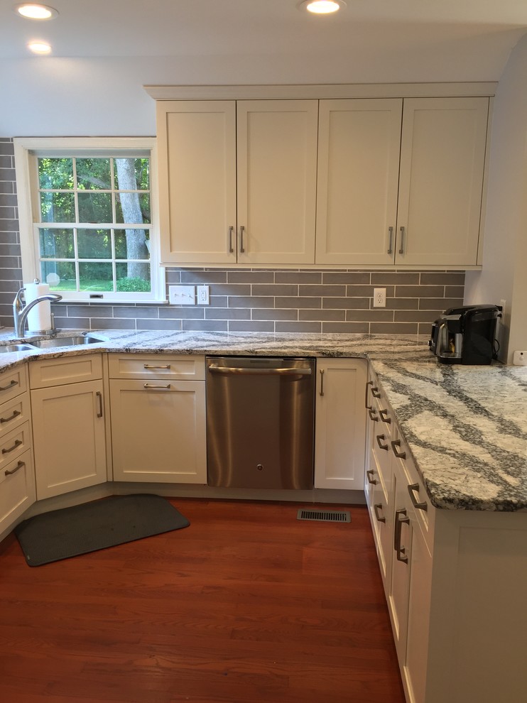 Inspiration for a mid-sized transitional u-shaped medium tone wood floor and red floor open concept kitchen remodel in Baltimore with a double-bowl sink, shaker cabinets, white cabinets, quartz countertops, gray backsplash, ceramic backsplash, stainless steel appliances, no island and gray countertops