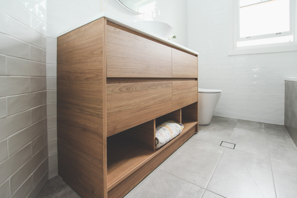 Design ideas for a mid-sized scandinavian master bathroom in Sydney with medium wood cabinets, a drop-in tub, a shower/bathtub combo, a two-piece toilet, white tile, white walls, porcelain floors, a console sink, grey floor, a hinged shower door, white benchtops, a single vanity and a freestanding vanity.