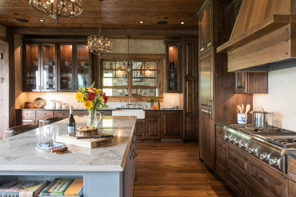 This is an example of a large country l-shaped eat-in kitchen in Minneapolis with a farmhouse sink, raised-panel cabinets, dark wood cabinets, granite benchtops, white splashback, stone tile splashback, panelled appliances, medium hardwood floors, with island and brown floor.