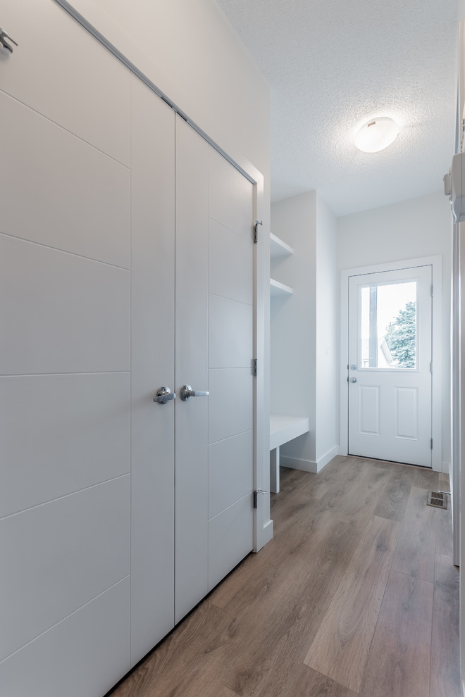 Design ideas for a small contemporary mudroom in Edmonton with white walls, laminate floors and brown floor.