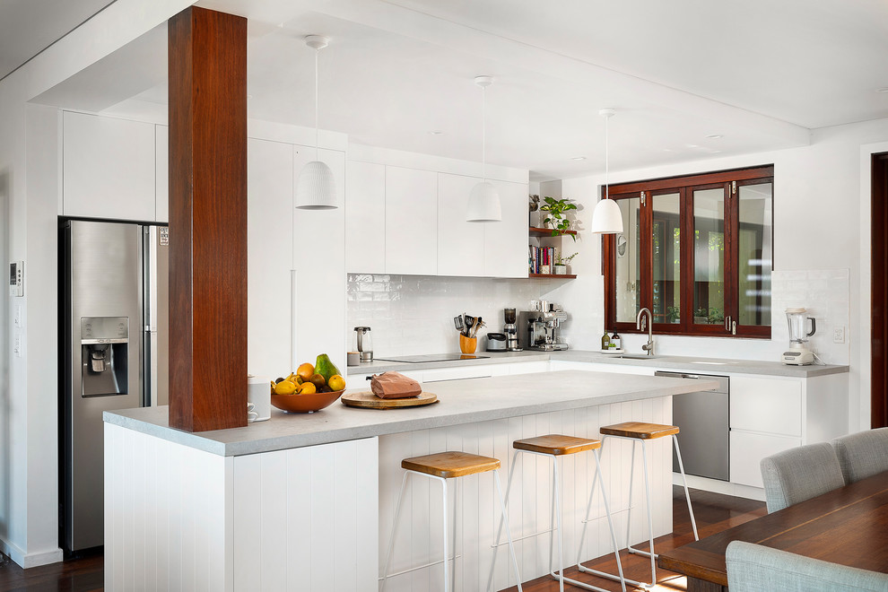 Large beach style l-shaped open plan kitchen in Sydney with an undermount sink, flat-panel cabinets, white cabinets, quartz benchtops, white splashback, subway tile splashback, stainless steel appliances, dark hardwood floors, with island, brown floor and grey benchtop.