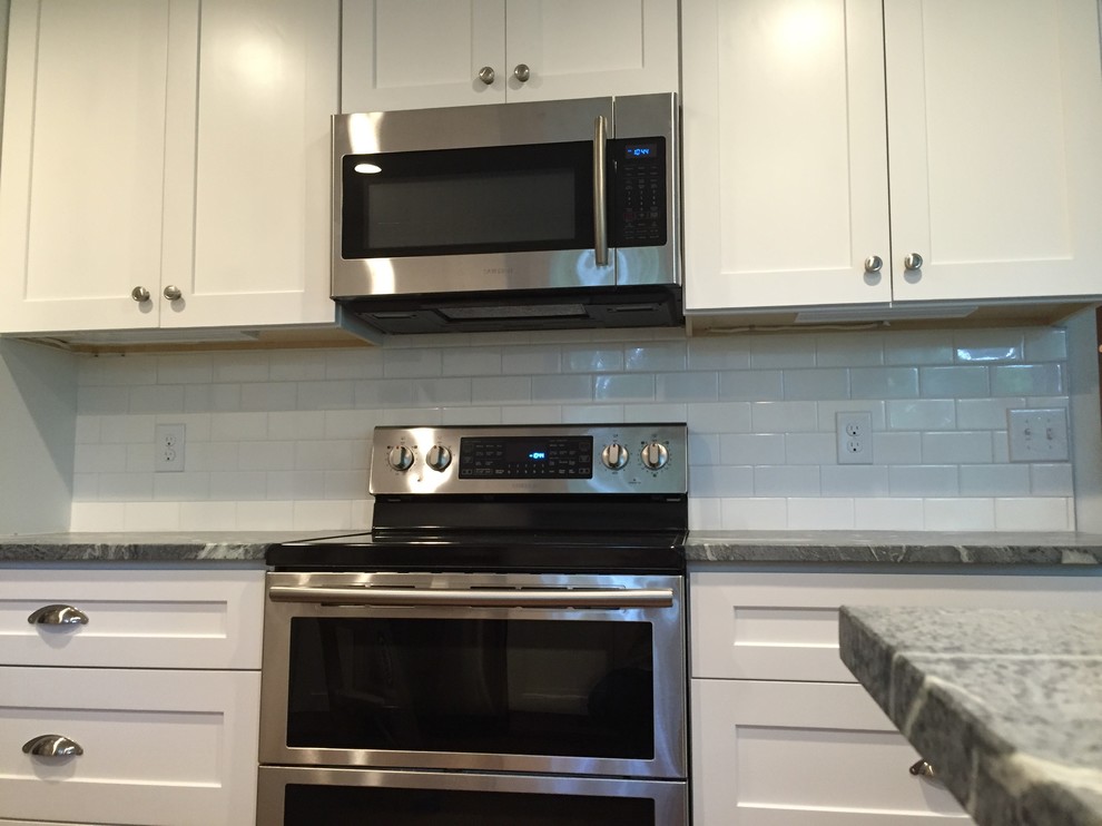 Example of a mid-sized transitional l-shaped medium tone wood floor enclosed kitchen design with an undermount sink, shaker cabinets, white cabinets, soapstone countertops, white backsplash, subway tile backsplash, stainless steel appliances and a peninsula