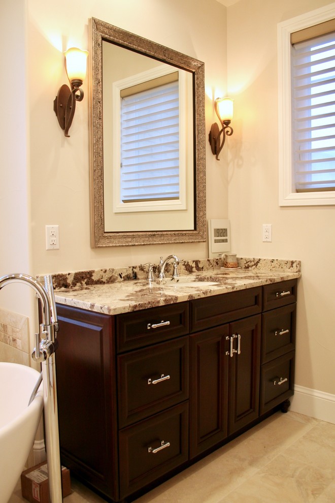 Photo of a mid-sized traditional master bathroom in Denver with raised-panel cabinets, dark wood cabinets, a freestanding tub, beige walls and an undermount sink.