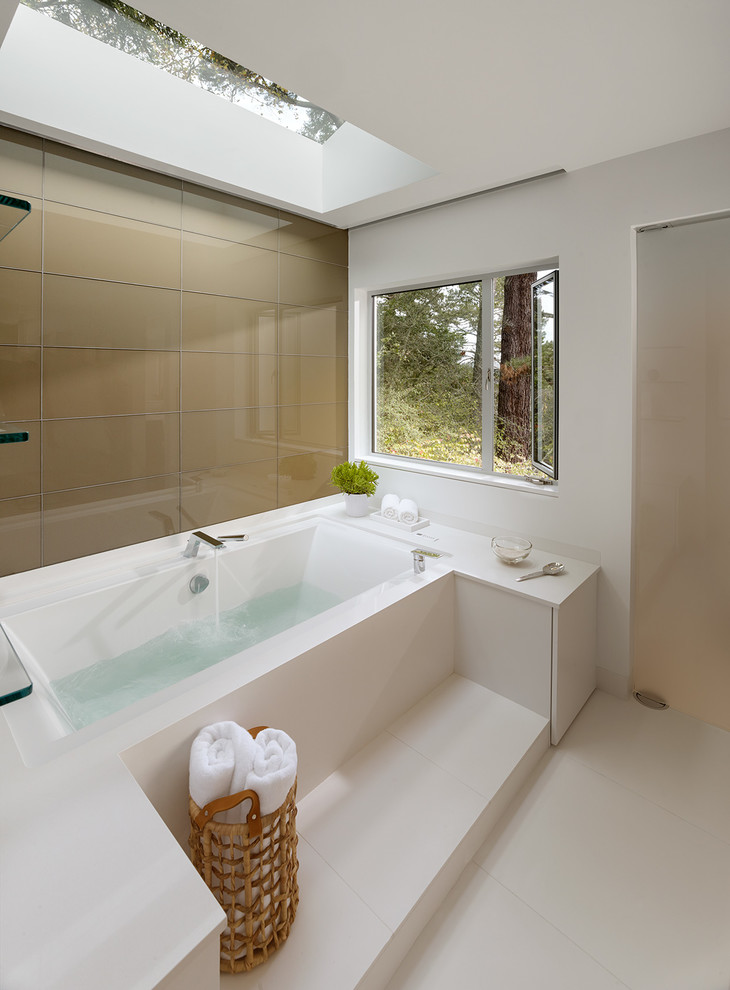 This is an example of a large contemporary master bathroom in San Francisco with white walls, flat-panel cabinets, white cabinets, an alcove tub, an alcove shower, a wall-mount toilet, white tile, porcelain tile, porcelain floors, an undermount sink and solid surface benchtops.