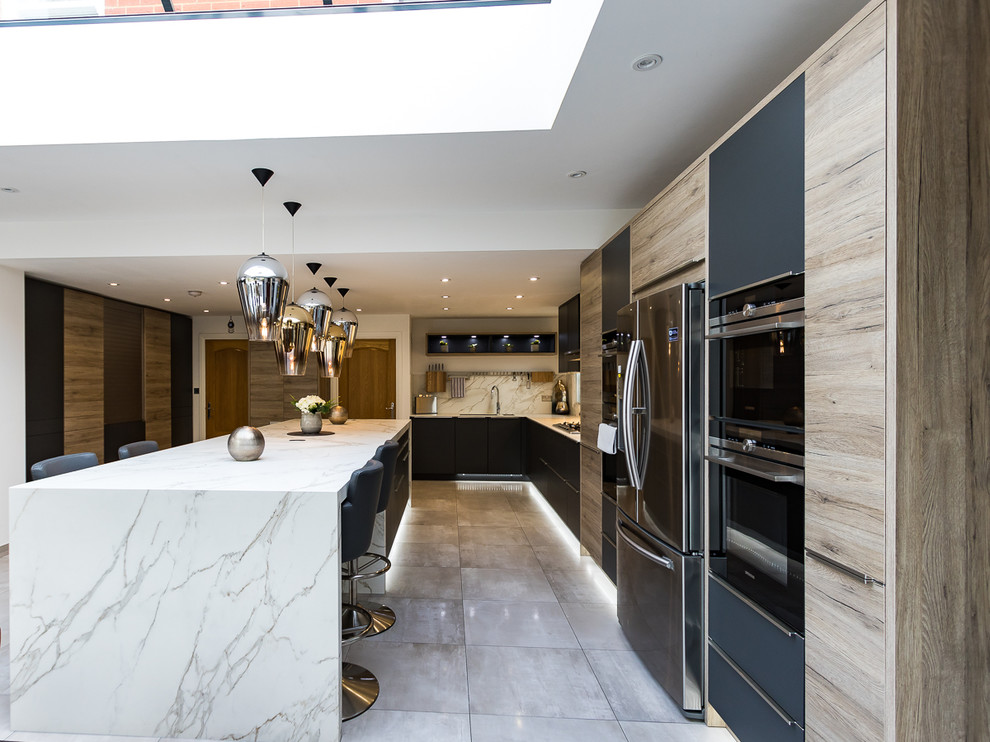 Large modern l-shaped open plan kitchen in Surrey with an integrated sink, flat-panel cabinets, grey cabinets, solid surface benchtops, white splashback, slate splashback, stainless steel appliances, porcelain floors, with island and grey floor.