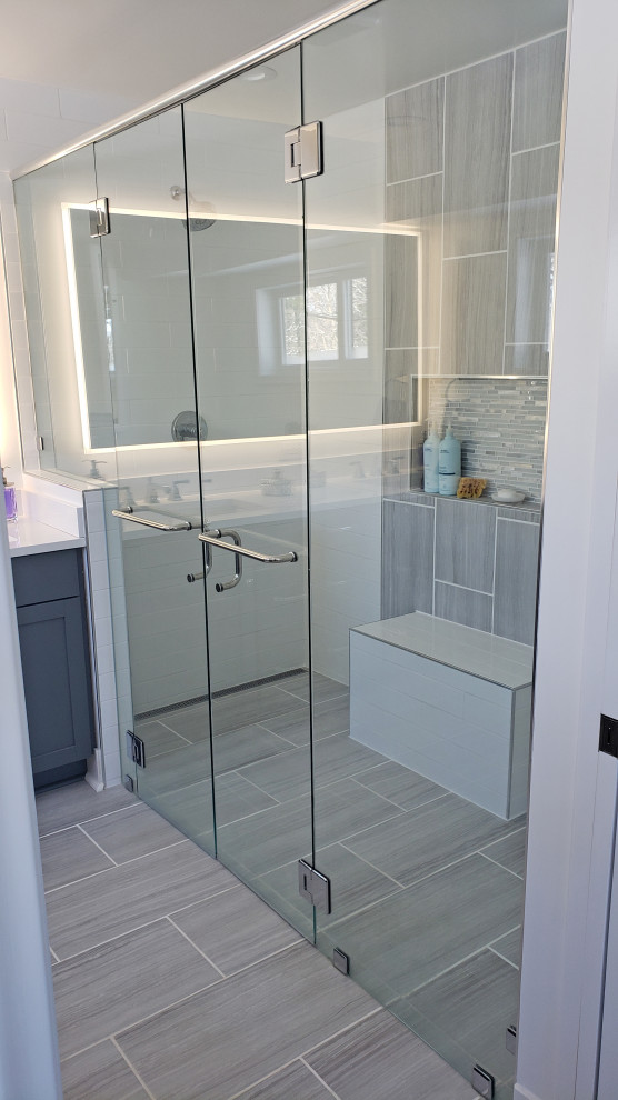 Walk-in shower - large transitional master gray tile and porcelain tile porcelain tile, gray floor and double-sink walk-in shower idea with shaker cabinets, gray cabinets, a two-piece toilet, white walls, an undermount sink, quartz countertops, a hinged shower door, white countertops and a built-in vanity