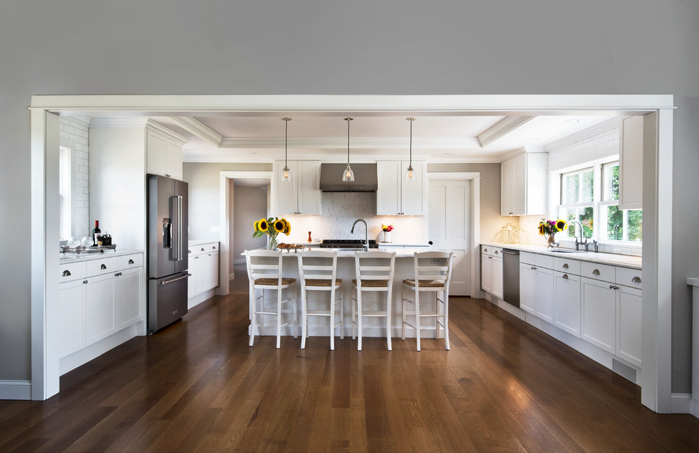 Large transitional u-shaped eat-in kitchen in New York with an undermount sink, shaker cabinets, white cabinets, quartz benchtops, white splashback, subway tile splashback, stainless steel appliances, dark hardwood floors, with island, brown floor and white benchtop.