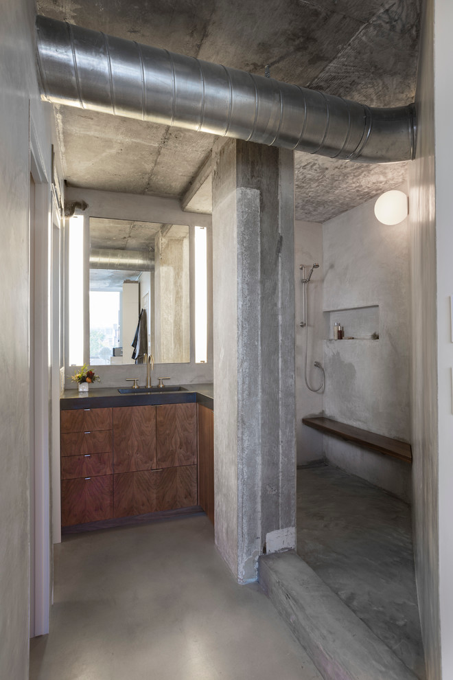 This is an example of a small industrial master bathroom in Austin with an integrated sink, flat-panel cabinets, dark wood cabinets, concrete benchtops, an open shower, a wall-mount toilet, grey walls and concrete floors.