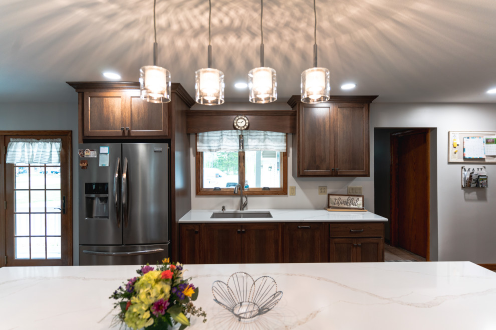 Example of a huge transitional l-shaped medium tone wood floor and brown floor open concept kitchen design with shaker cabinets, medium tone wood cabinets, quartz countertops, stainless steel appliances, an island, white countertops and an undermount sink