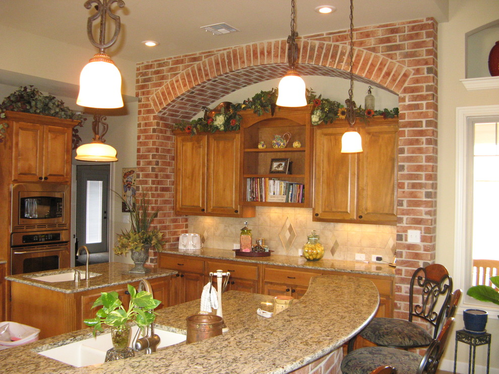 This is an example of a large traditional u-shaped eat-in kitchen with medium wood cabinets, granite benchtops, beige splashback, stainless steel appliances, multiple islands, an undermount sink, recessed-panel cabinets, cement tile splashback, travertine floors, beige floor and beige benchtop.
