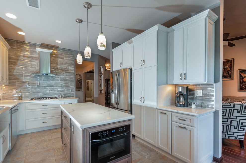 Mid-sized transitional l-shaped porcelain tile and multicolored floor enclosed kitchen photo in Philadelphia with a farmhouse sink, shaker cabinets, white cabinets, quartzite countertops, brown backsplash, stone tile backsplash, stainless steel appliances, an island and white countertops