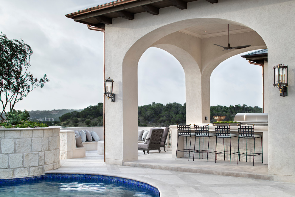 This is an example of an expansive transitional backyard patio in Austin with an outdoor kitchen and a roof extension.