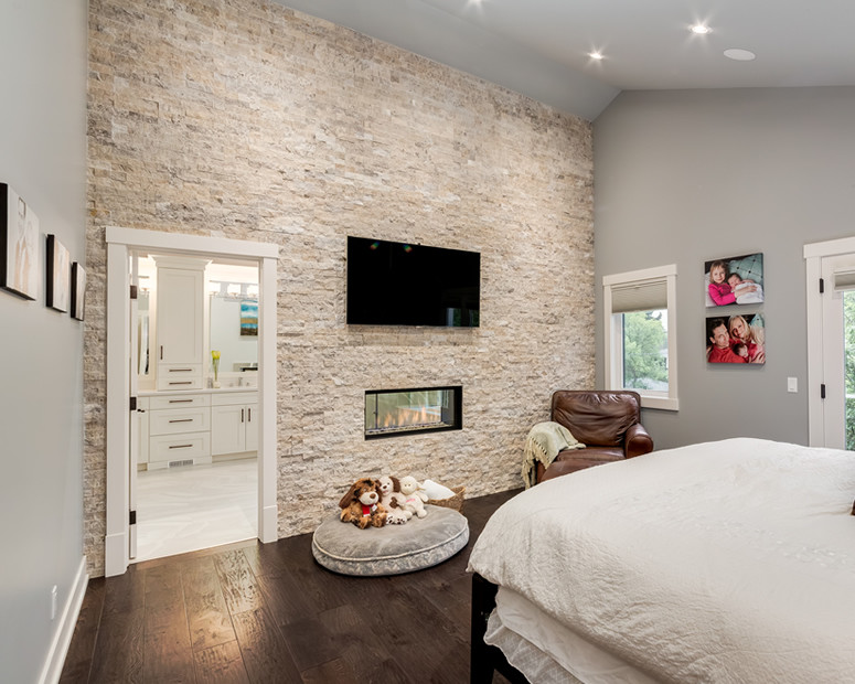 Mid-sized modern master bedroom in Calgary with grey walls, dark hardwood floors, a two-sided fireplace, a stone fireplace surround and brown floor.