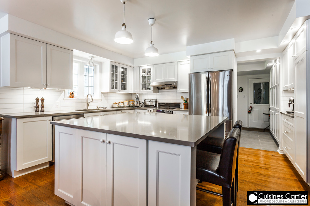 Eat-in kitchen - large transitional medium tone wood floor eat-in kitchen idea in Montreal with a double-bowl sink, shaker cabinets, white cabinets, quartzite countertops, white backsplash, ceramic backsplash, stainless steel appliances and an island