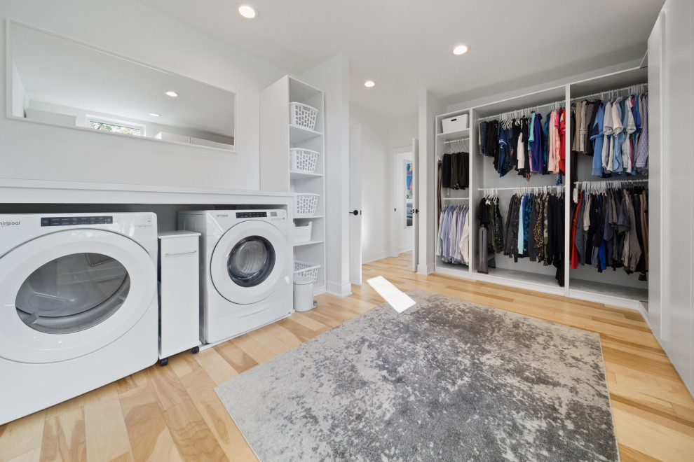 Design ideas for a large modern single-wall laundry cupboard in Kansas City with white cabinets, white walls, light hardwood floors and a side-by-side washer and dryer.