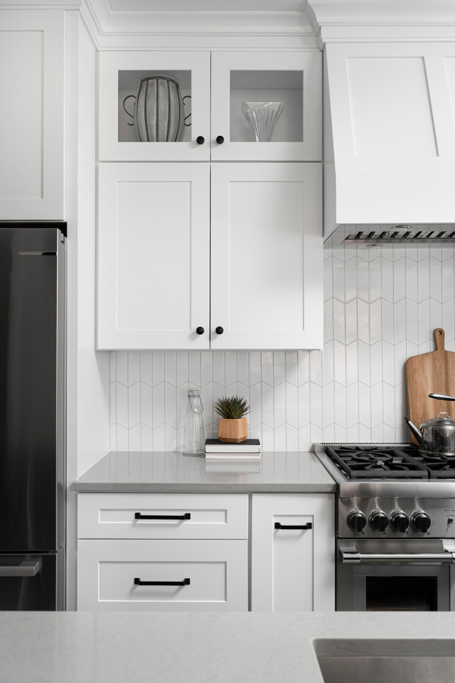Example of a mid-sized transitional galley light wood floor open concept kitchen design in Chicago with an undermount sink, shaker cabinets, white cabinets, quartz countertops, white backsplash, ceramic backsplash, stainless steel appliances, an island and gray countertops