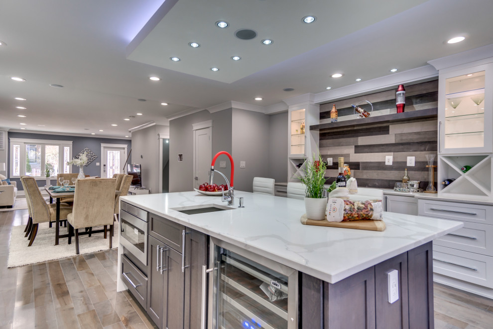Large modern l-shaped kitchen/diner in DC Metro with a built-in sink, shaker cabinets, white cabinets, marble worktops, grey splashback, mosaic tiled splashback, stainless steel appliances, plywood flooring, an island, grey floors and white worktops.