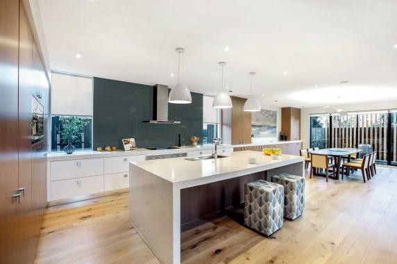 This is an example of an expansive contemporary l-shaped kitchen pantry with an undermount sink, flat-panel cabinets, white cabinets, quartz benchtops, blue splashback, stainless steel appliances, light hardwood floors, with island and glass sheet splashback.