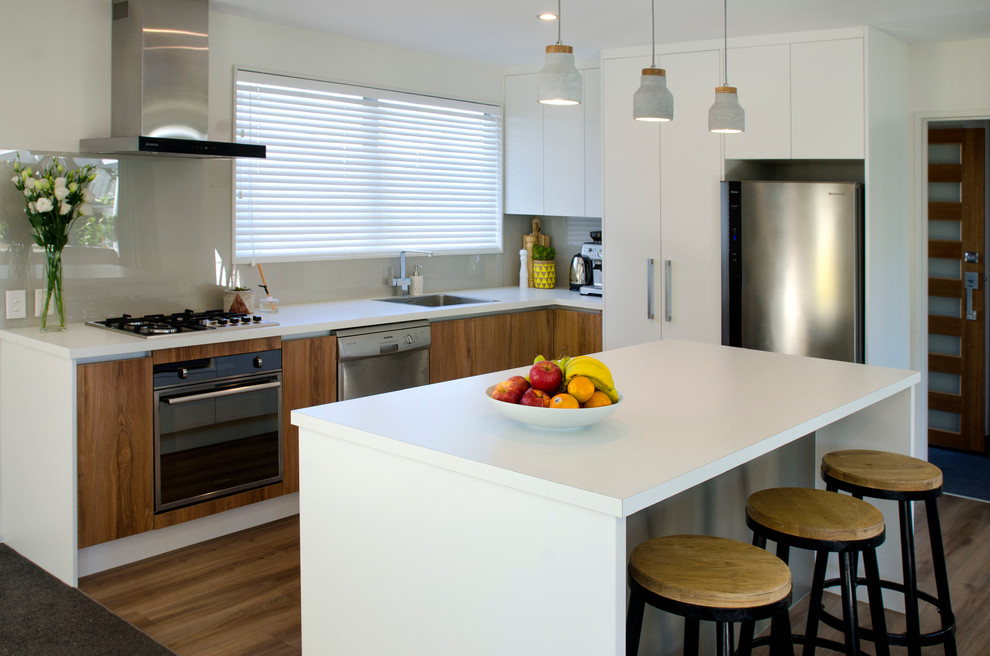 Design ideas for a large contemporary l-shaped eat-in kitchen in Christchurch with a single-bowl sink, flat-panel cabinets, medium wood cabinets, laminate benchtops, grey splashback, glass sheet splashback, stainless steel appliances, vinyl floors, with island, brown floor and white benchtop.