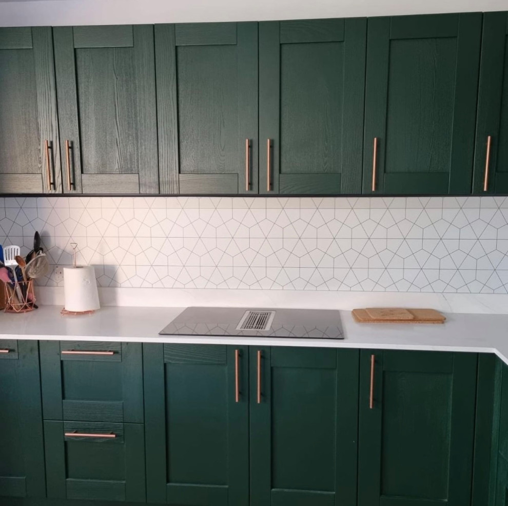 Medium sized u-shaped open plan kitchen in Surrey with a submerged sink, shaker cabinets, green cabinets, marble worktops, multi-coloured splashback, stone tiled splashback, black appliances, an island and white worktops.