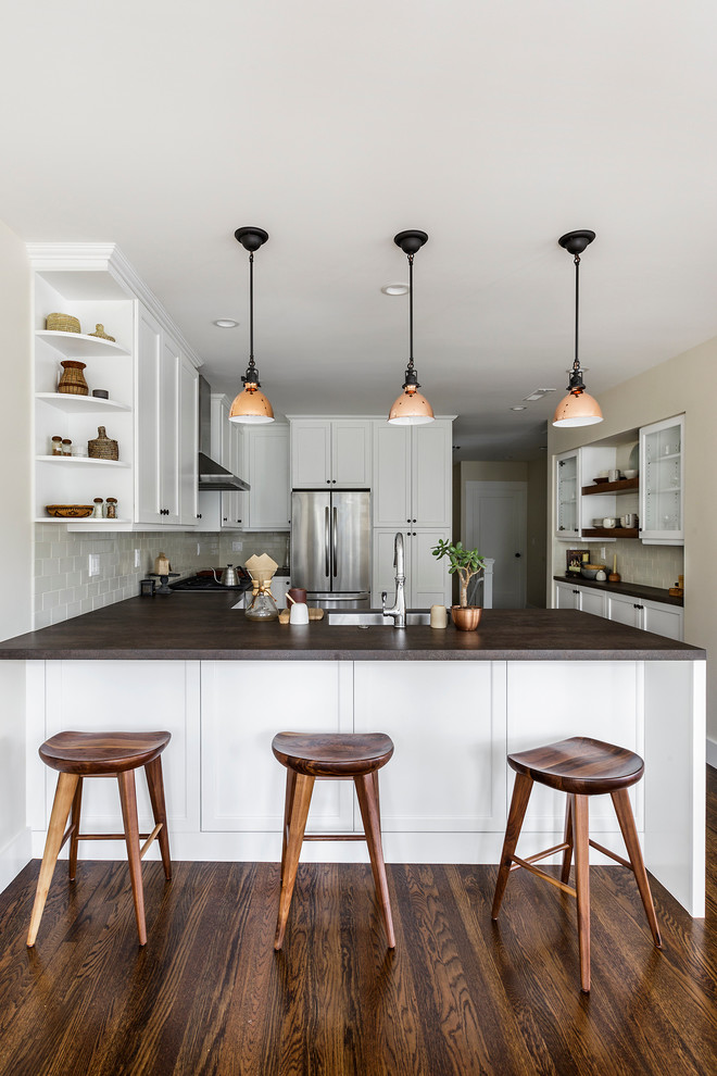 Inspiration for a mid-sized traditional u-shaped eat-in kitchen in San Francisco with a single-bowl sink, shaker cabinets, white cabinets, solid surface benchtops, beige splashback, ceramic splashback, stainless steel appliances, medium hardwood floors, a peninsula and brown benchtop.