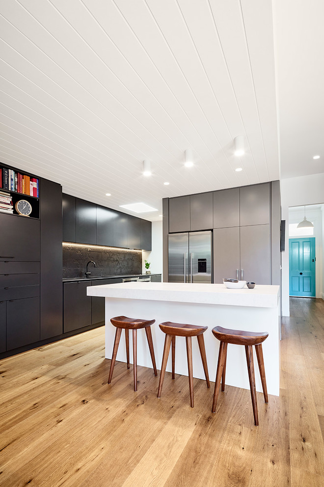 Photo of a contemporary galley kitchen in Melbourne with flat-panel cabinets, black cabinets, stainless steel appliances, light hardwood floors and with island.