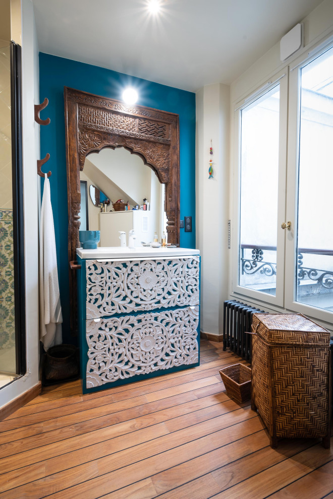 This is an example of a mid-sized tropical master bathroom in Paris with beaded inset cabinets, turquoise cabinets, an alcove shower, blue tile, ceramic tile, white walls, dark hardwood floors, a trough sink, solid surface benchtops, brown floor, white benchtops, a laundry, a single vanity and a freestanding vanity.