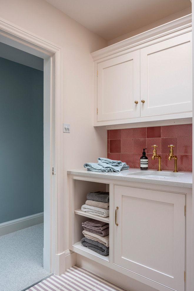 Enclosed kitchen - transitional ceramic tile and pink floor enclosed kitchen idea in Buckinghamshire with shaker cabinets, pink cabinets, solid surface countertops, pink backsplash, ceramic backsplash, white appliances, an island, white countertops and an undermount sink