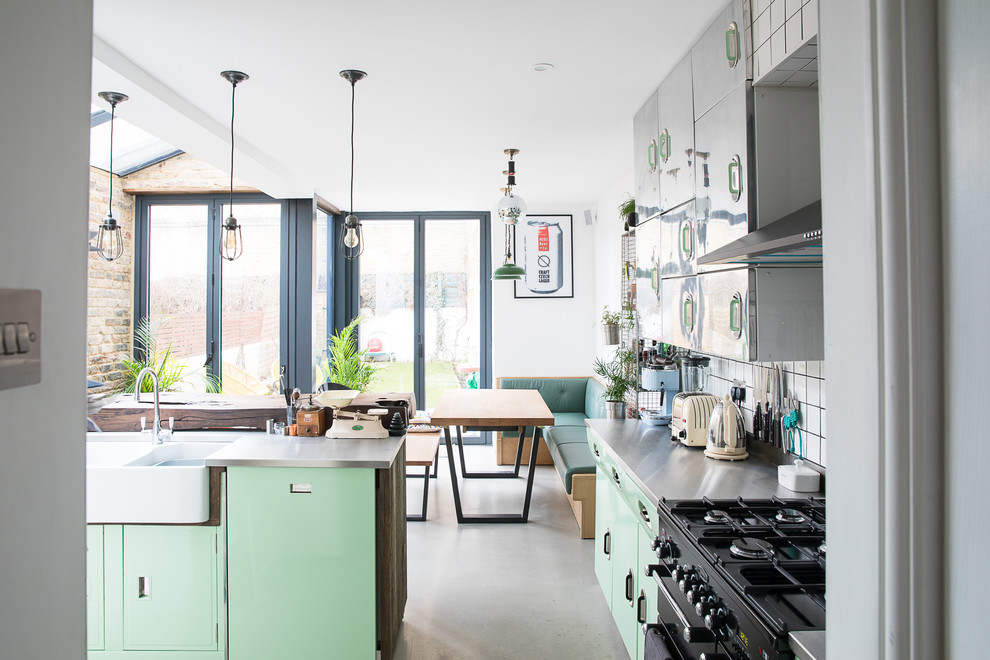Design ideas for a large industrial kitchen in London with green cabinets, stainless steel benchtops, concrete floors, with island, grey floor and grey benchtop.