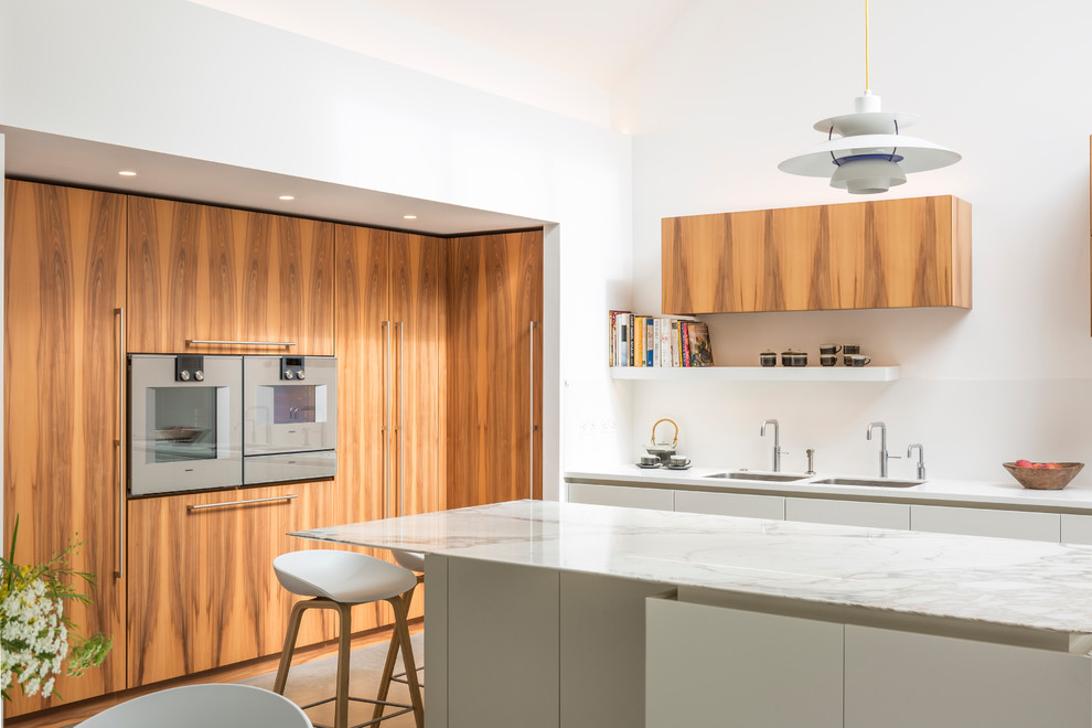 This is an example of a large contemporary kitchen in London with a double-bowl sink, flat-panel cabinets, marble benchtops, white splashback, with island, grey floor, white benchtop and medium wood cabinets.