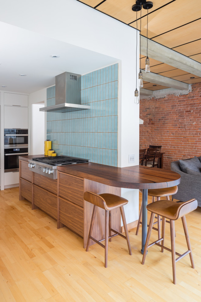 Cette image montre une cuisine urbaine en U et bois brun avec un placard à porte plane, une péninsule, un plan de travail bleu, un électroménager en acier inoxydable, parquet clair et un sol beige.