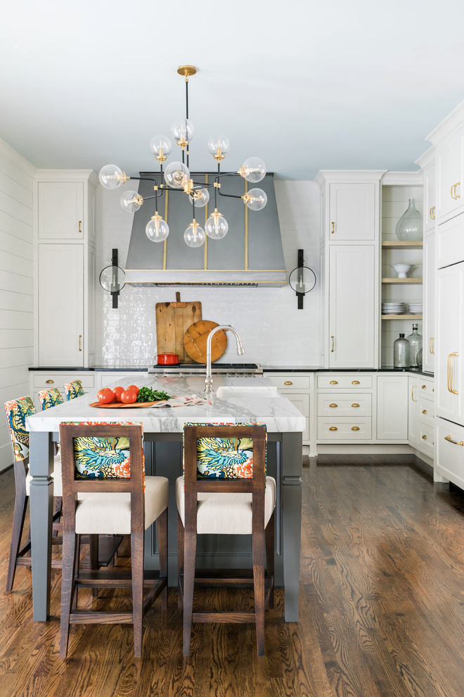 Design ideas for a transitional l-shaped kitchen in Atlanta with a farmhouse sink, beaded inset cabinets, white cabinets, white splashback, subway tile splashback, panelled appliances, dark hardwood floors, with island, brown floor and black benchtop.