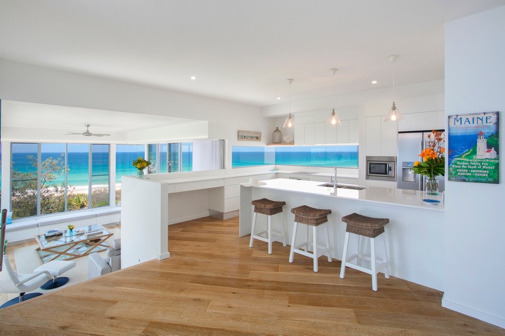 Beach style l-shaped open plan kitchen in Sunshine Coast with an undermount sink, flat-panel cabinets, white cabinets, stainless steel appliances, medium hardwood floors and a peninsula.