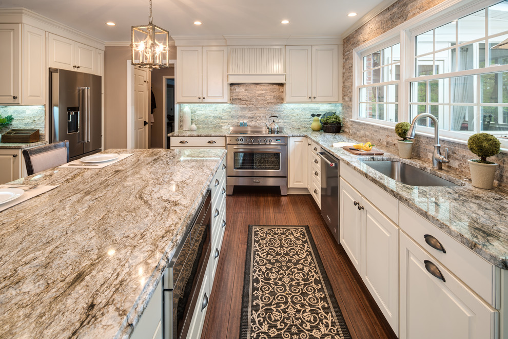 Photo of a large traditional u-shaped eat-in kitchen in Atlanta with an undermount sink, raised-panel cabinets, white cabinets, granite benchtops, brick splashback, stainless steel appliances, bamboo floors, with island, brown floor, brown splashback and multi-coloured benchtop.