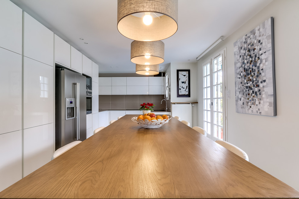 This is an example of a large contemporary l-shaped eat-in kitchen in Paris with flat-panel cabinets, white cabinets, grey splashback and stainless steel appliances.